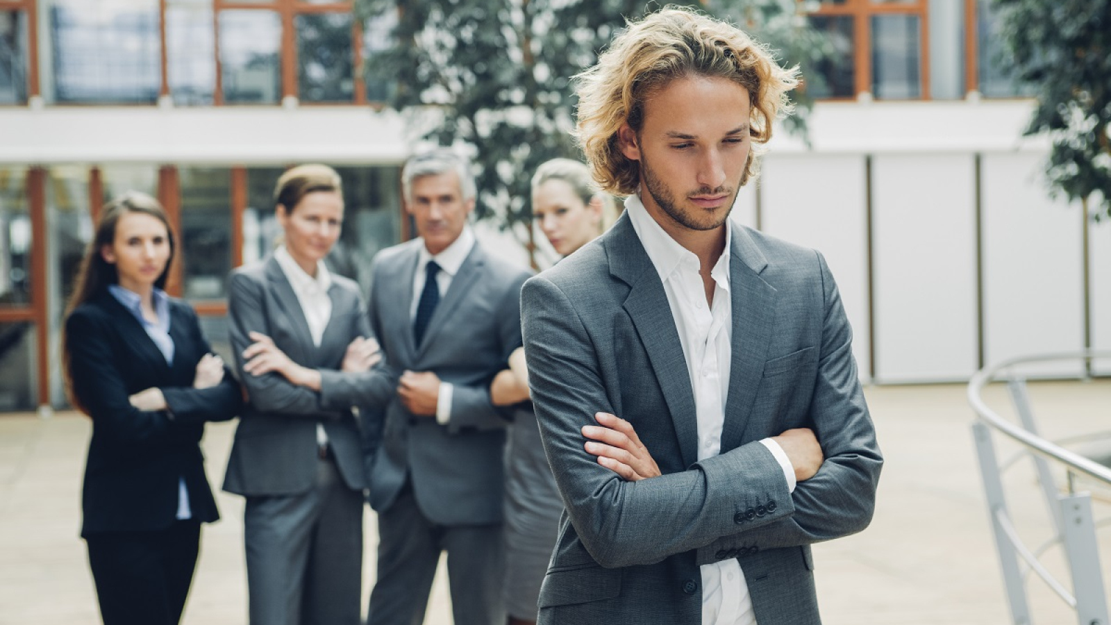 Businessman with crossed arms, excluded from group of business people