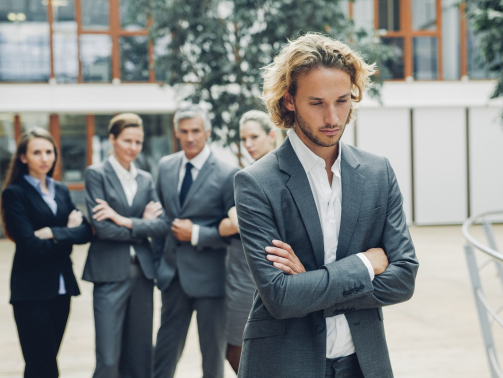 Businessman with crossed arms, excluded from group of business people